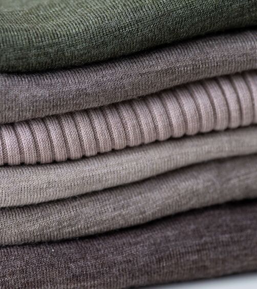 A stack of folded, textured knit sweaters in muted earth tones creates a cozy, layered appearance.